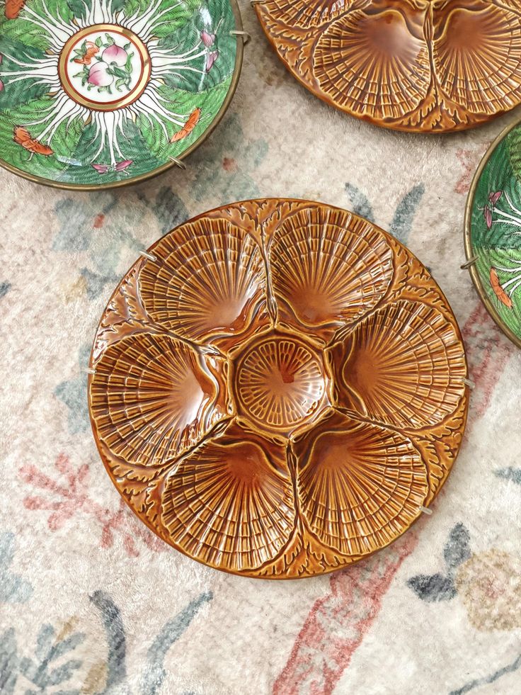 three decorative plates sitting on top of a table next to an orange flowered plate