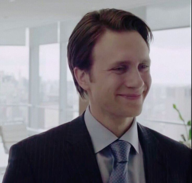 a man wearing a suit and tie in an office building smiling at the camera while looking off into the distance