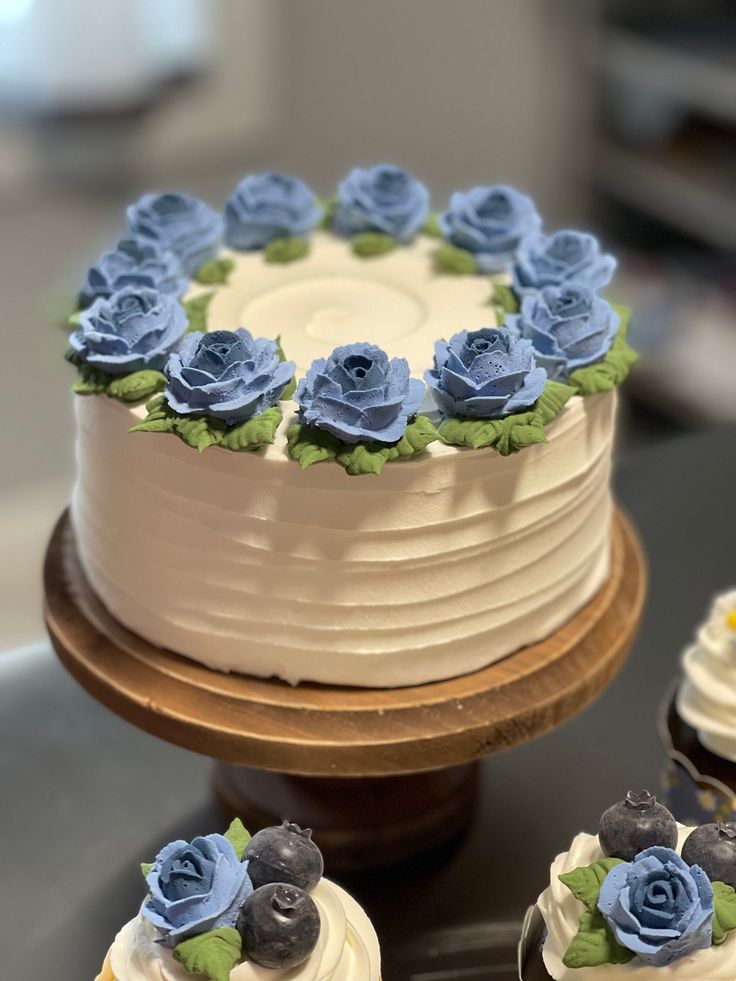 a cake with frosting and blue flowers is on a table next to other cupcakes