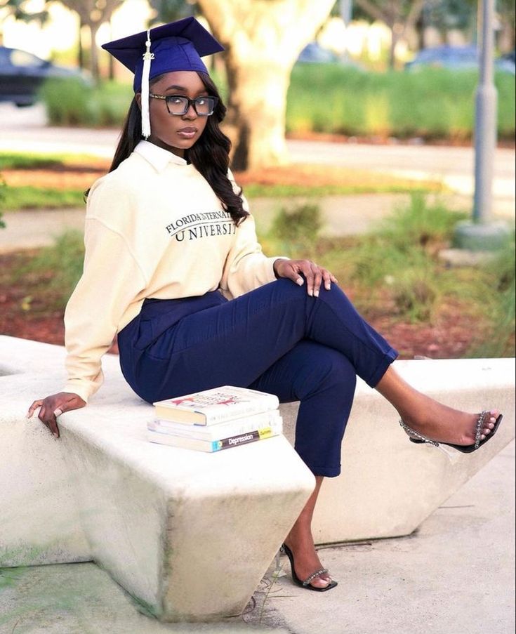 a woman sitting on top of a cement bench wearing a graduation cap and blue pants