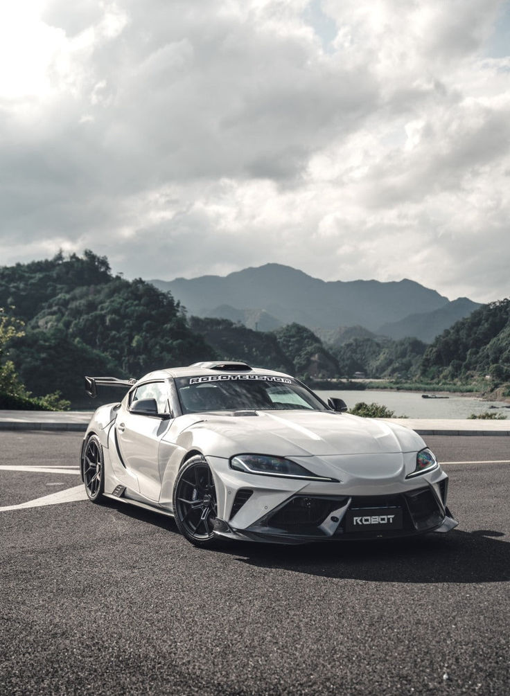 a white sports car parked in a parking lot with mountains in the backgroud