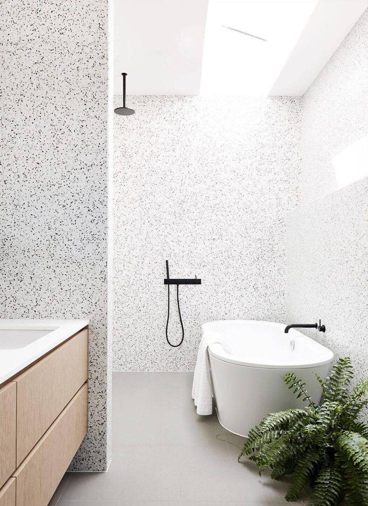 a white bath tub sitting under a window next to a green leafy plant in a bathroom