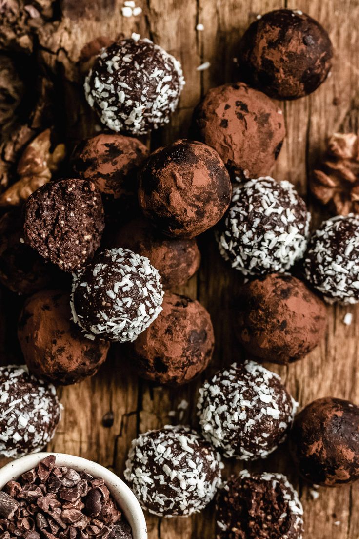 chocolate truffles on a wooden table next to a white bowl filled with nuts