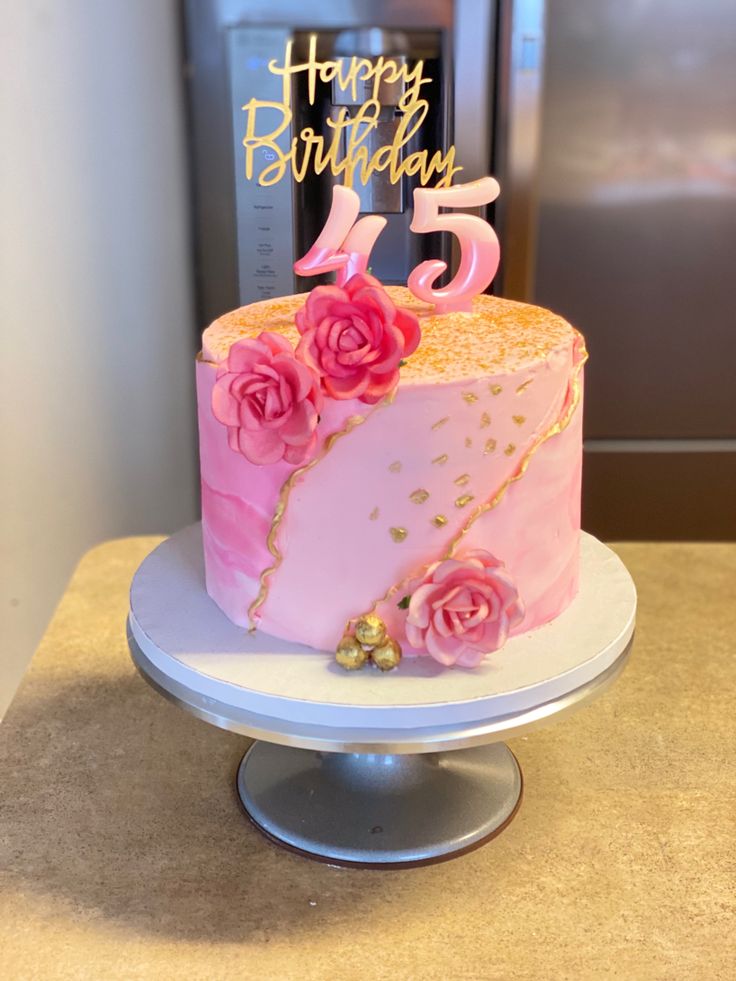 a birthday cake with pink frosting and flowers on top is sitting on a table