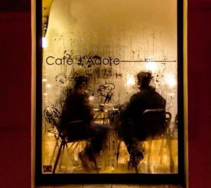 two people sitting at a table in front of a window with the words cafe adore written on it