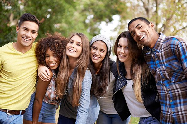 a group of young people standing next to each other in front of trees and grass