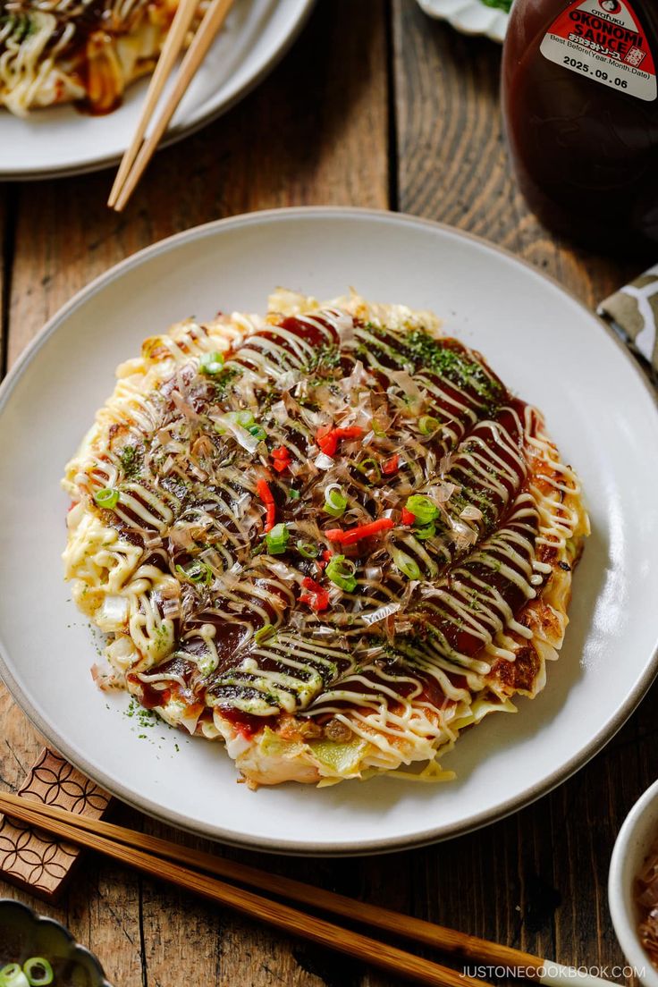 a white plate topped with noodles covered in sauce and toppings next to chopsticks