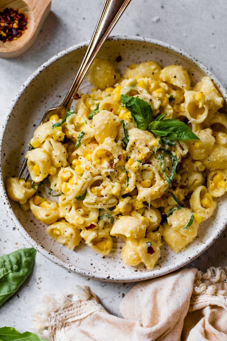 a white bowl filled with macaroni and cheese on top of a table next to a wooden spoon