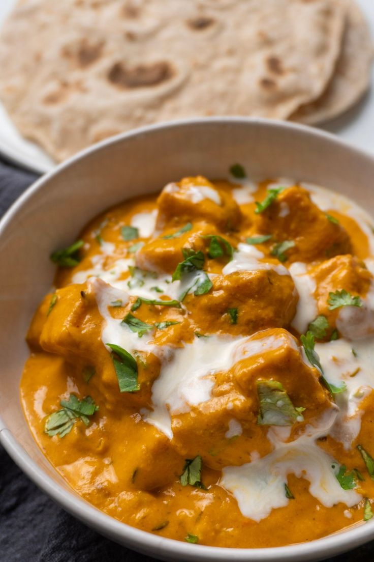 a white bowl filled with food next to some pita bread on a black cloth