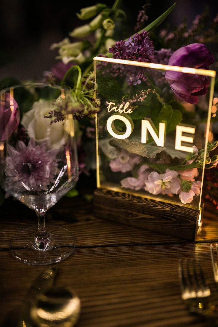 the table is set with purple flowers and gold place card holders, along with silverware