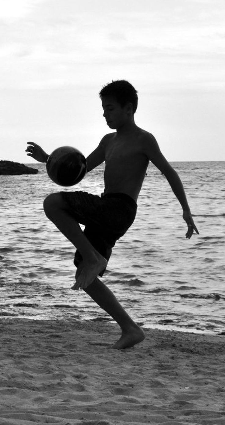 a young man is playing with a ball on the beach in front of the ocean