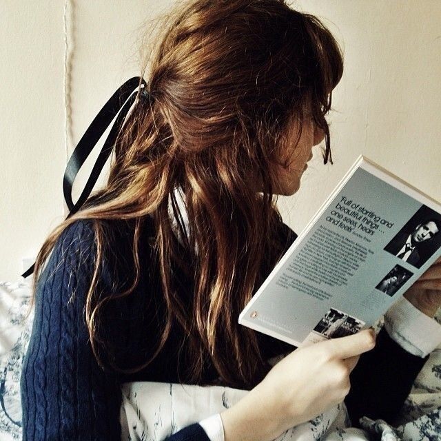 a woman reading a book while sitting on a bed with her hair blowing in the wind