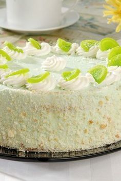 a cake with white frosting and green toppings on a plate next to a coffee cup