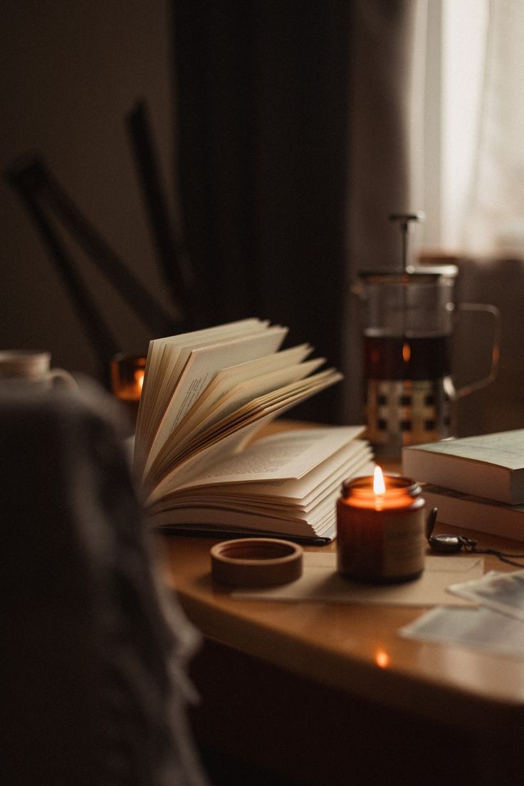 an open book sitting on top of a wooden table next to a candle and some books