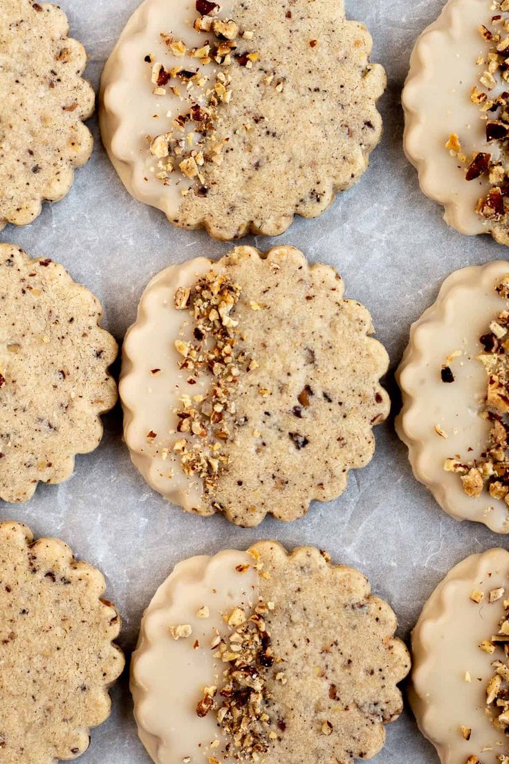 twelve cookies with white frosting and nuts on top