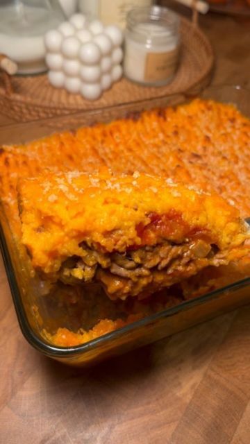 a casserole dish with meat, cheese and sauce in it on a wooden table