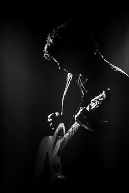 a black and white photo of a man playing an acoustic guitar in the dark with spotlights behind him