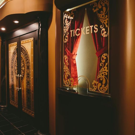 an entrance to a theater with red curtains and gold lettering on the front door, along with black tile flooring