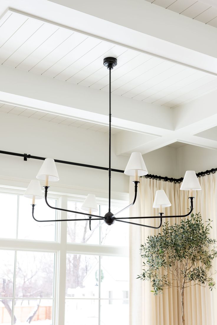 a chandelier hanging from the ceiling in a living room with windows and curtains