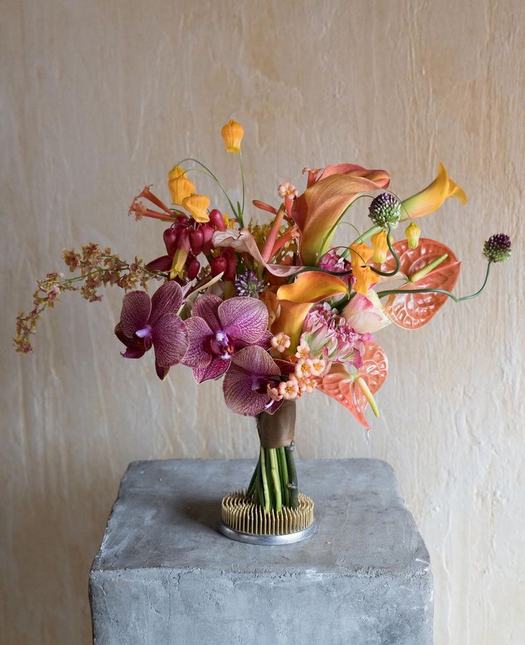 a vase filled with lots of colorful flowers on top of a cement block in front of a wall