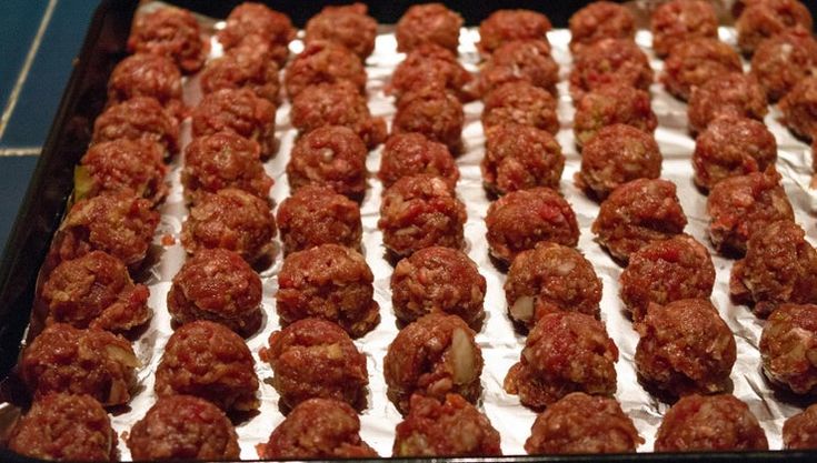 meatballs are covered in white icing and sitting on a baking sheet, ready to go into the oven