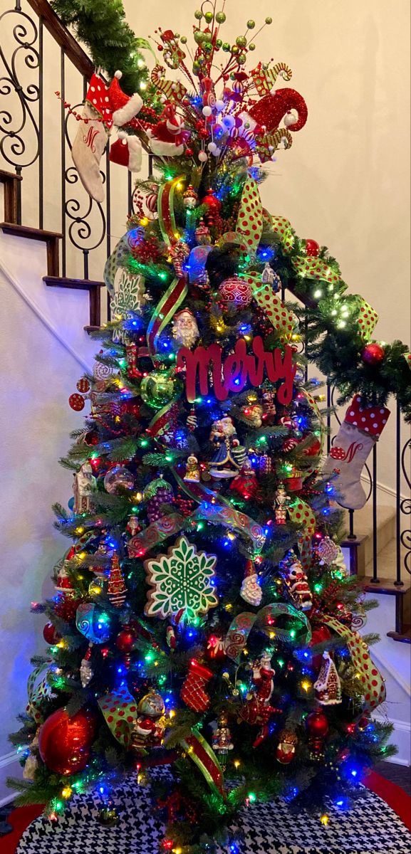 a christmas tree decorated with ornaments and lights on the bottom of a set of stairs