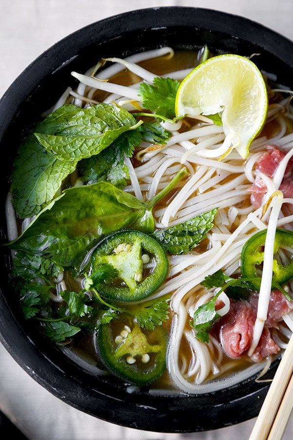 a black bowl filled with noodles, meat and veggies next to chopsticks