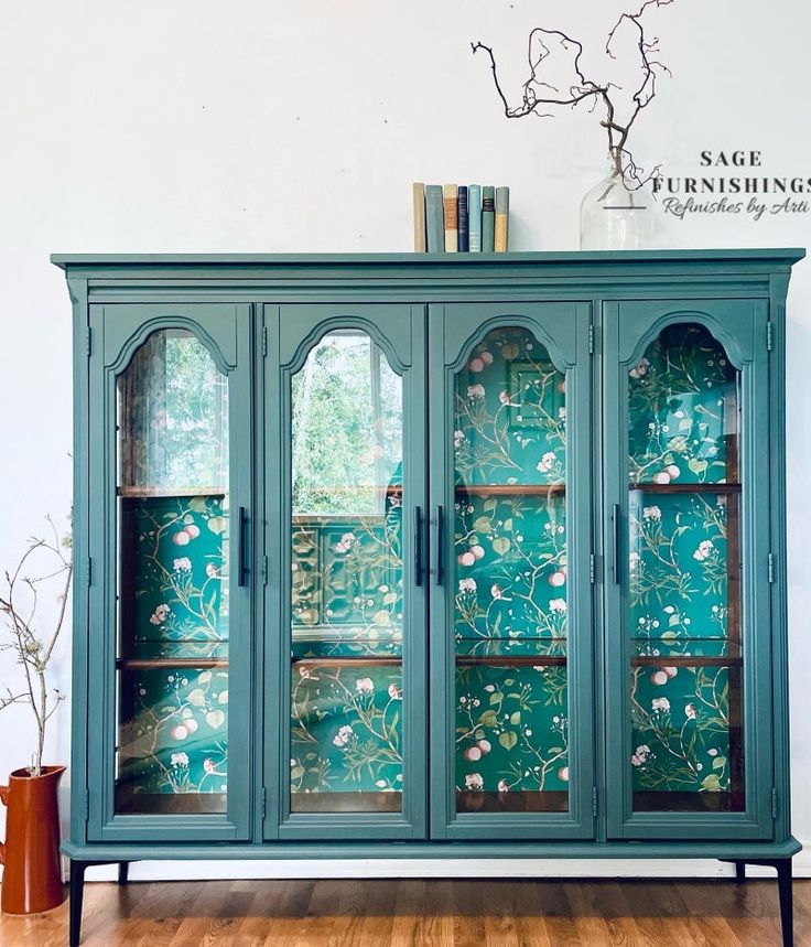 a green china cabinet with glass doors and flowers on it