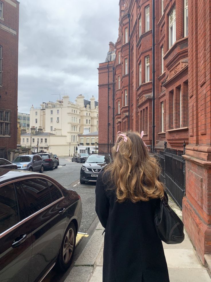 a woman is walking down the street with her back to the camera and looking at cars