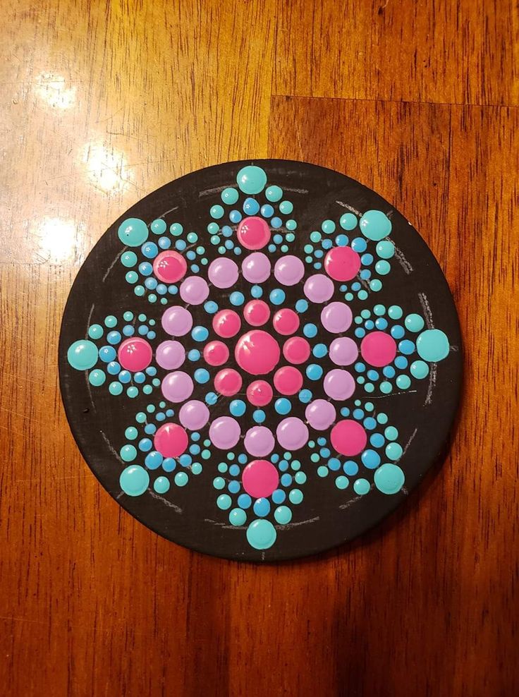 a black plate with pink, blue and green dots on it sitting on a wooden table