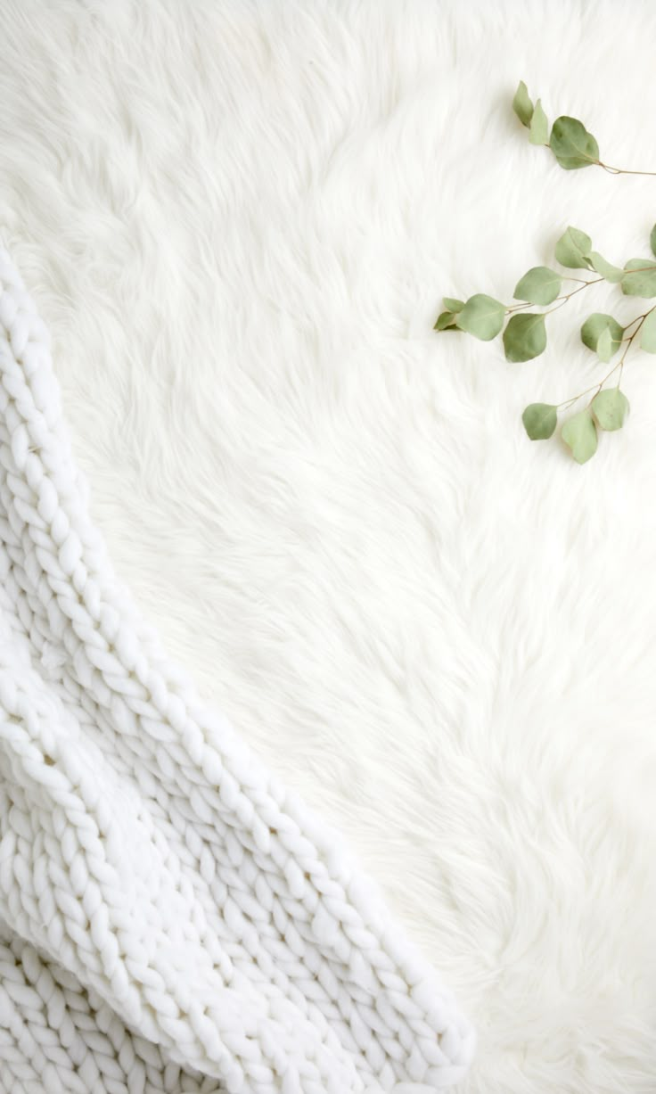 a white blanket and some green leaves on top of it next to a cup of coffee