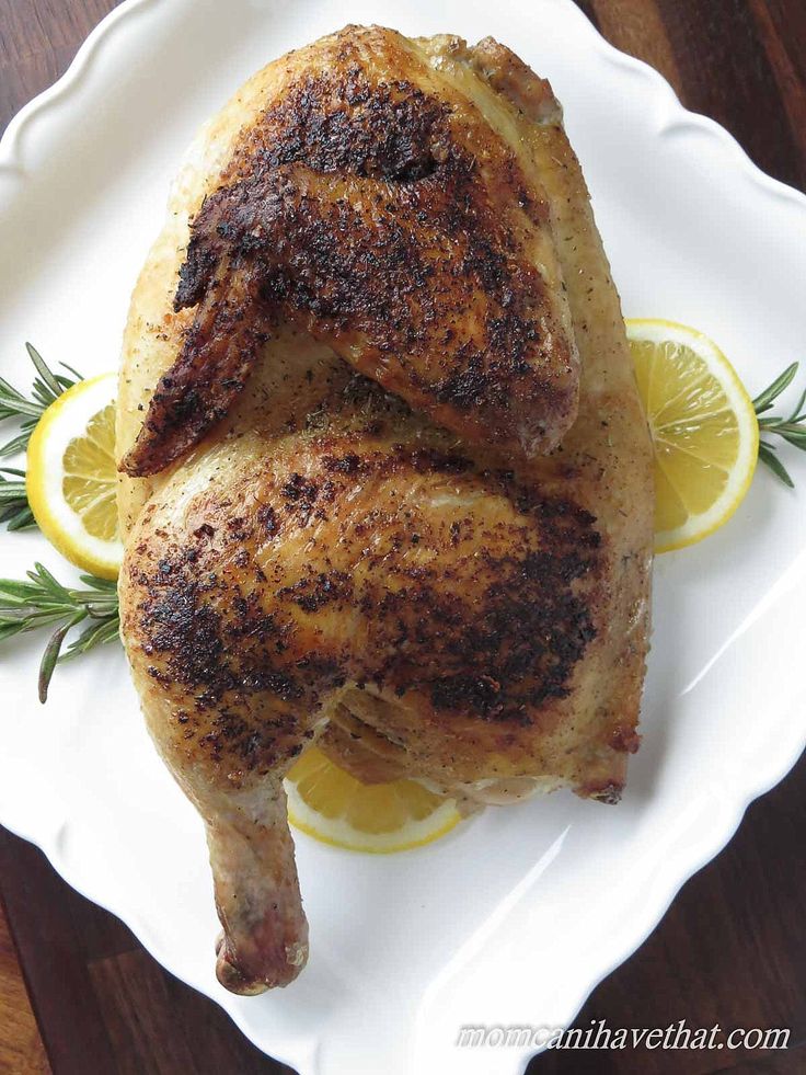 a whole chicken on a plate with lemons and rosemary