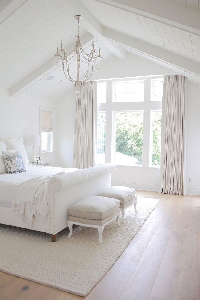 a large white bed sitting in a bedroom next to a chandelier and window