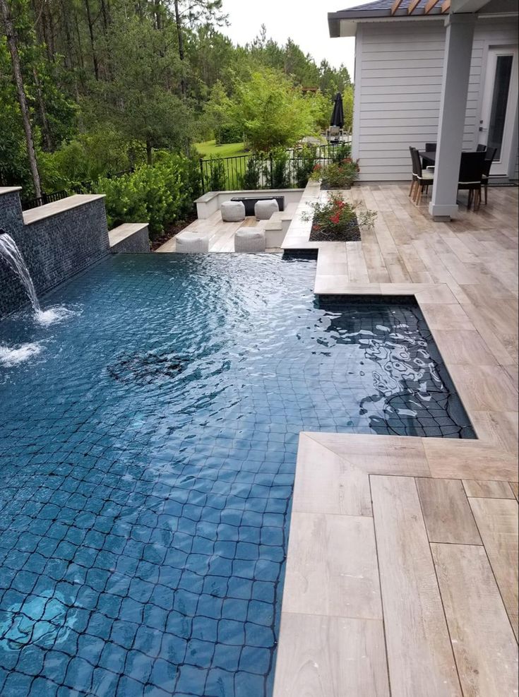 an outdoor swimming pool with waterfall and patio furniture in the backround, surrounded by greenery