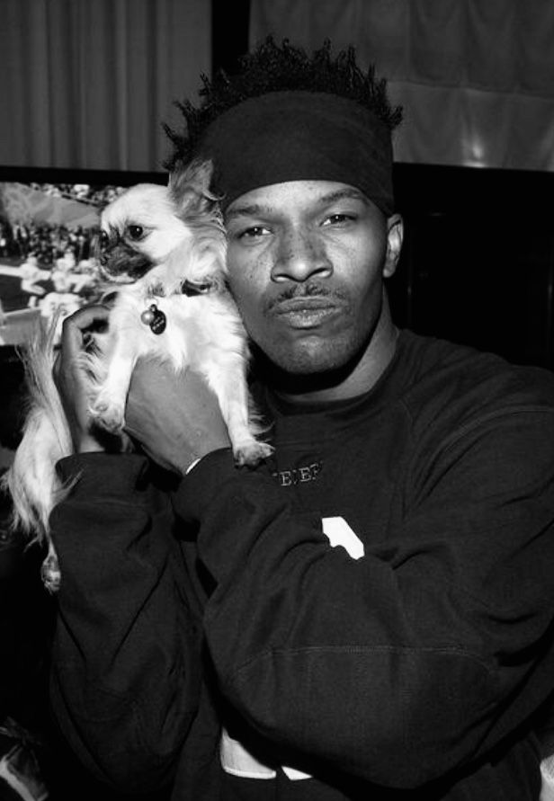 a man holding a small white dog in his lap while wearing a hat and sweater