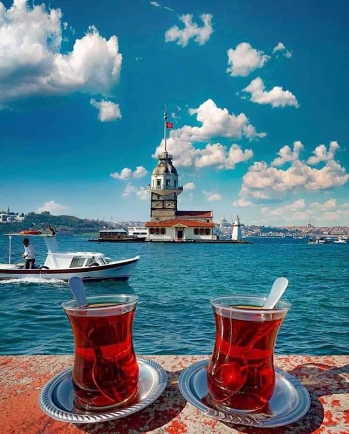 two cups of tea sitting on top of a table next to the ocean with boats in the background