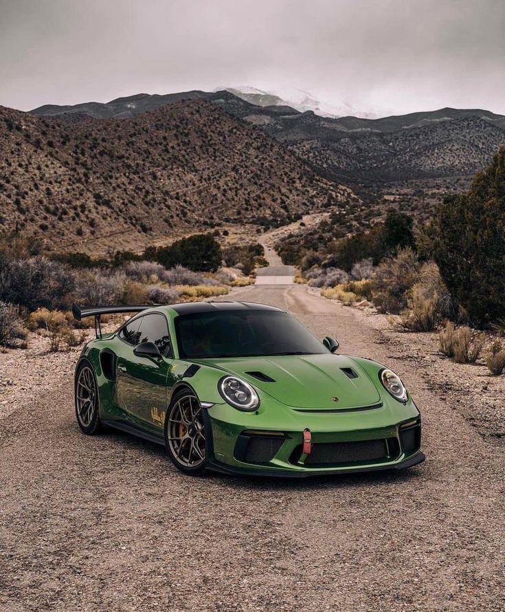 a green sports car parked on the side of a dirt road in front of mountains