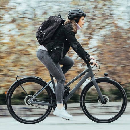 a woman riding a bike down the street with a backpack on her back and helmet on