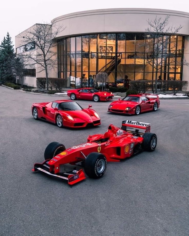 four red race cars parked in front of a building