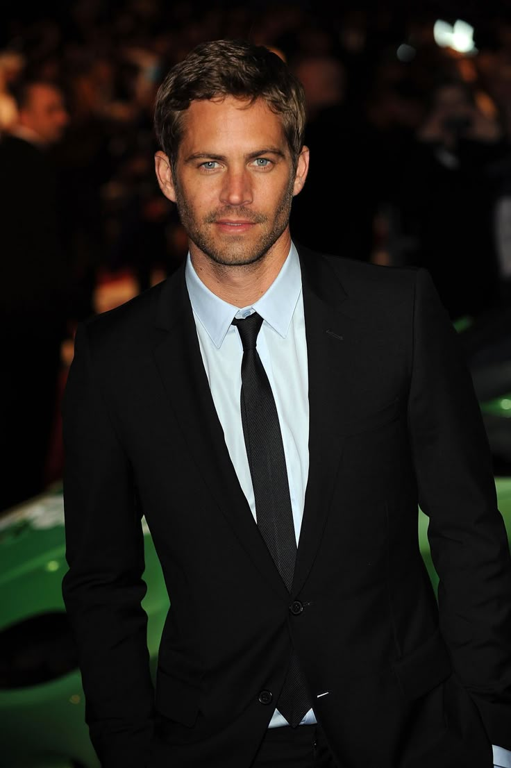 a man in a suit and tie standing next to a green car at an event