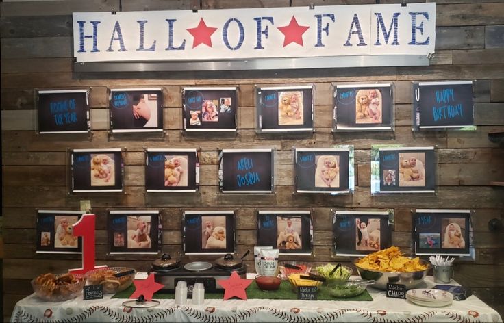 a table topped with pictures and food on top of a wooden paneled wall next to a sign that says hall of fame