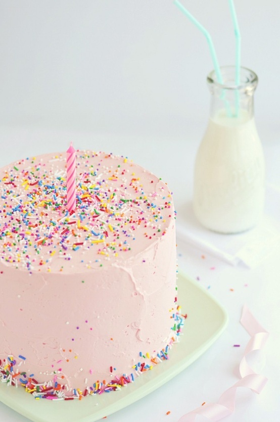 a pink birthday cake with sprinkles and a single candle on the top