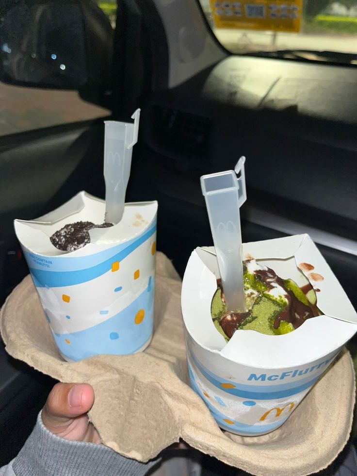 two ice cream cones with toppings in the back seat of a car, being held up by someone's hand