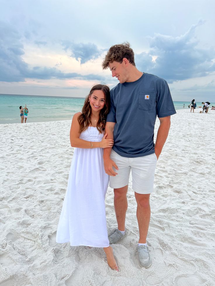 a man standing next to a woman on top of a sandy beach