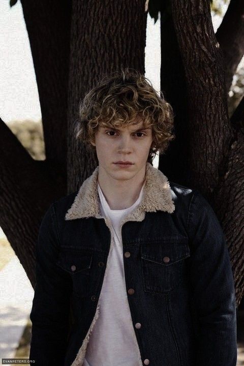 a young man standing in front of a tree wearing a denim jacket and white shirt