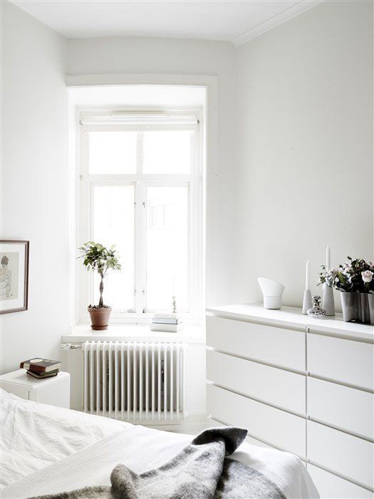 a bedroom with white walls and flooring has plants on the window sill next to the bed