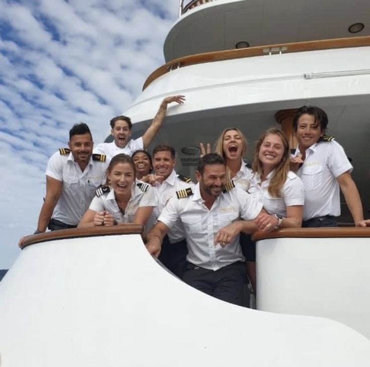 a group of people standing on the side of a boat posing for a photo with their hands in the air