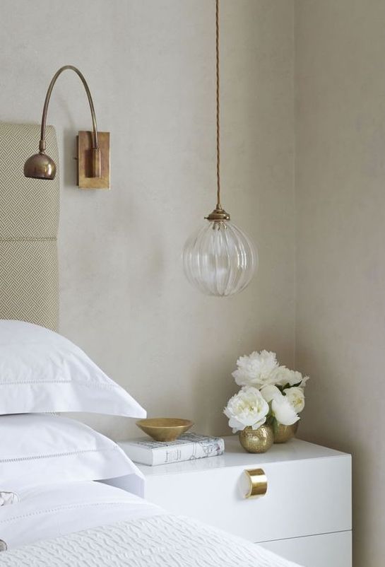 a white bed sitting next to a nightstand with flowers on it and a lamp hanging from the wall