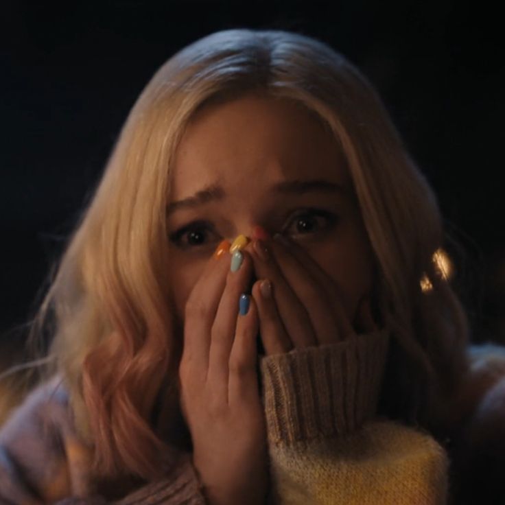 a woman covering her face with both hands and looking at the camera while standing in front of some lights