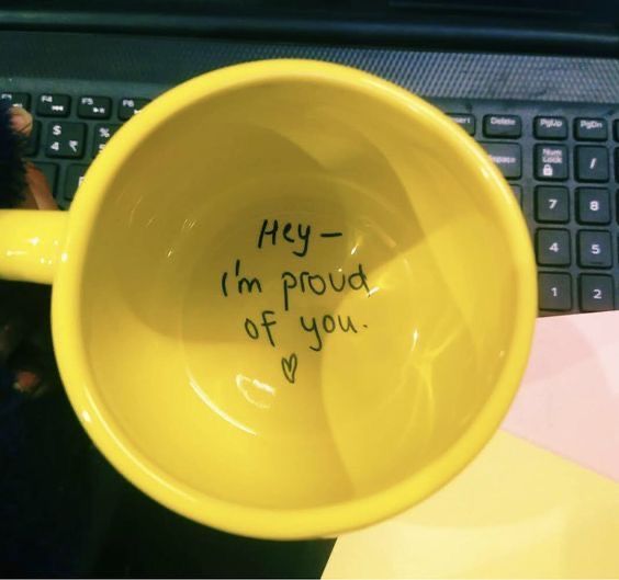 a yellow coffee cup with writing on it sitting next to a computer keyboard that says hey i'm proud of you